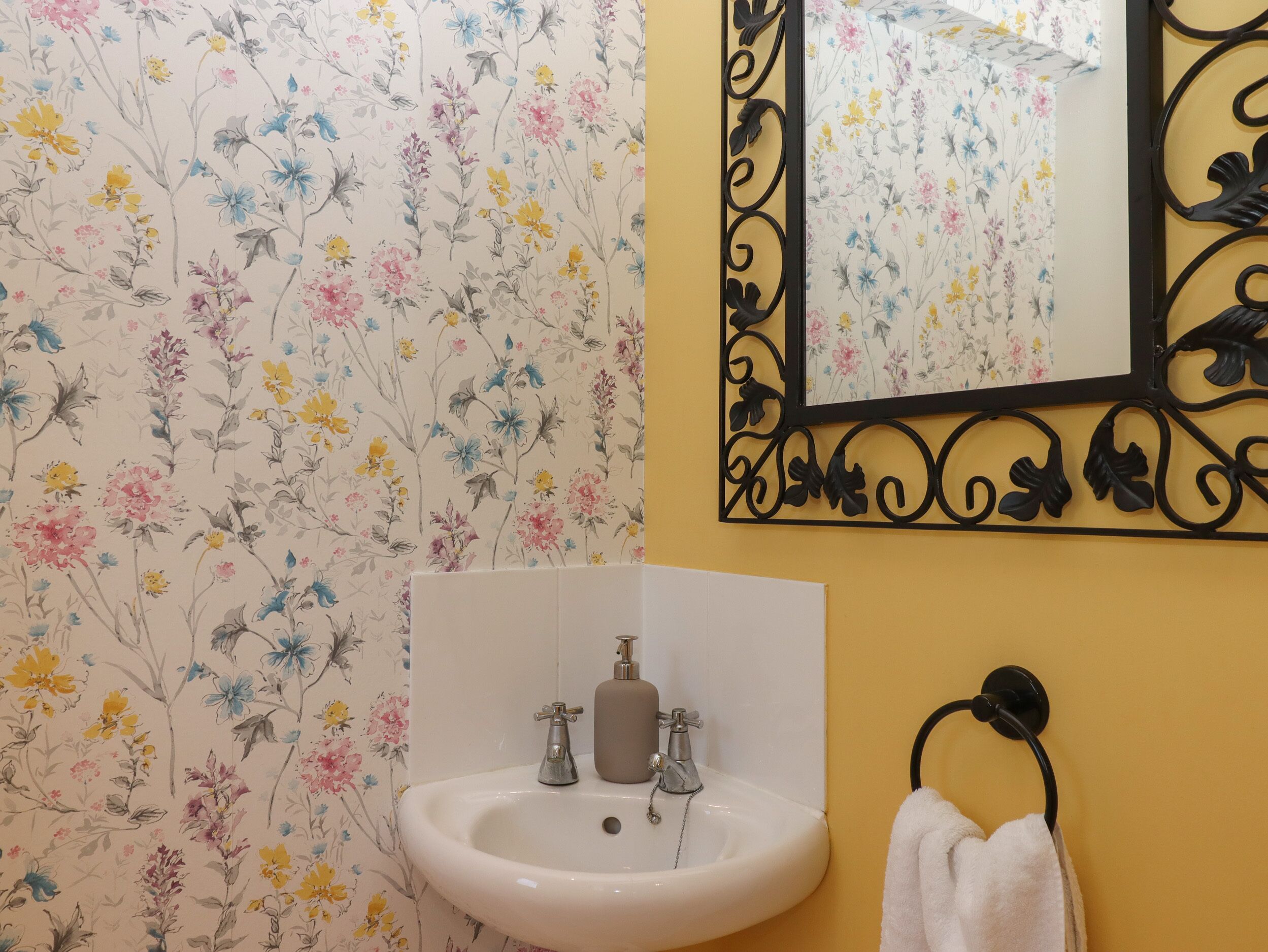 A bathroom with a floral wallpaper, a white sink, a mirror with a black frame, and a towel rack.