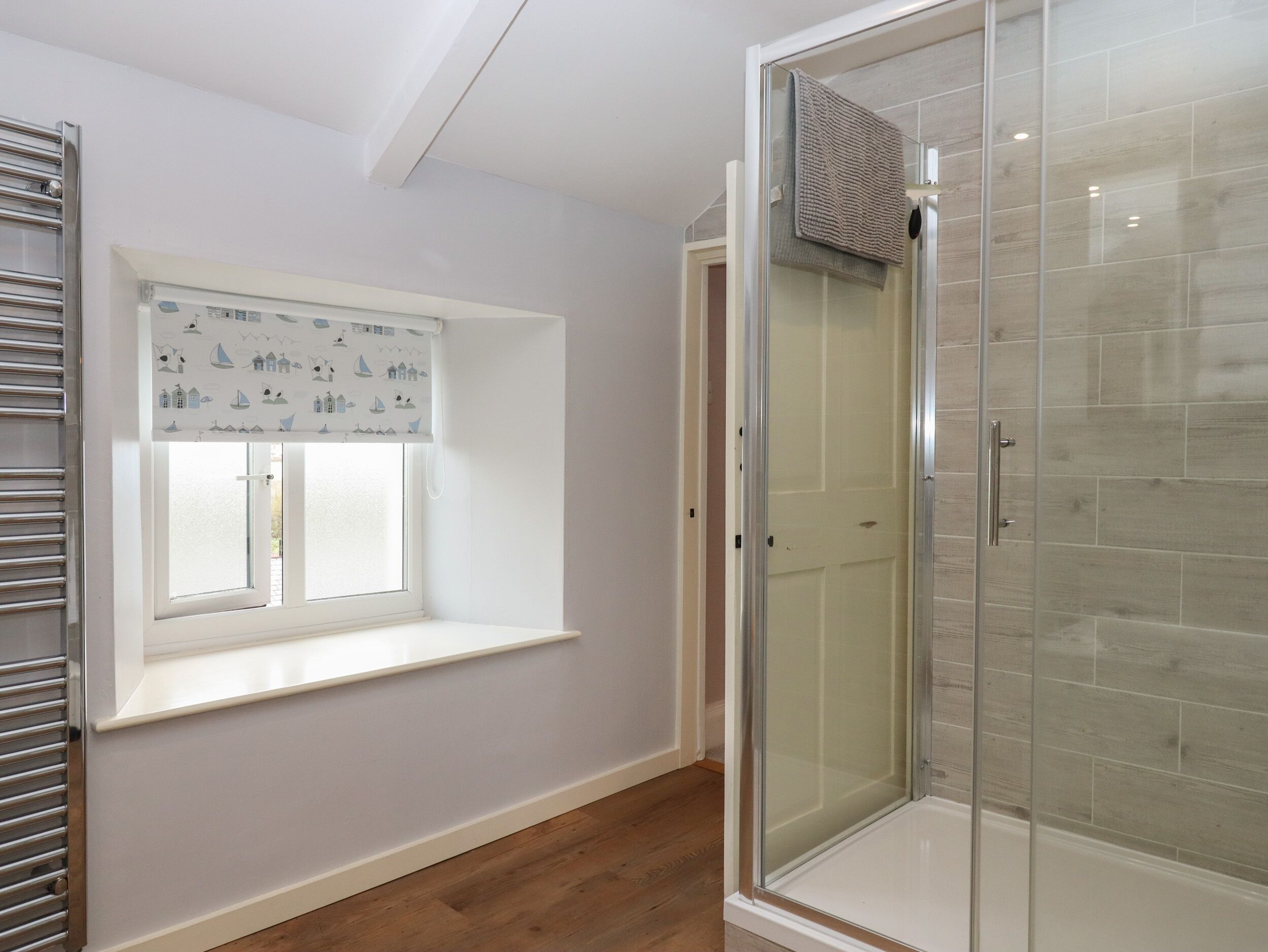 A bathroom with a glass shower enclosure, a window with a white frame, and a towel hanging on the shower door.