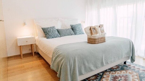 Een keurig opgemaakt slaapkamer met een bed, nachtkastje en een mand met spullen op het bed.