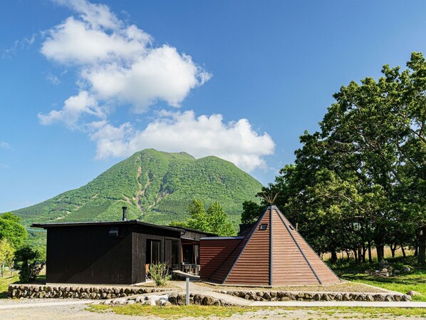 A lodge with a wooden cabin and a pyramid-shaped structure, surrounded by lush greenery and a mountain in the background.