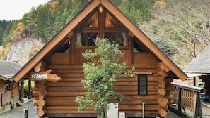 Une cabane en rondins avec un toit triangulaire, une enseigne en bois et un petit arbre devant.