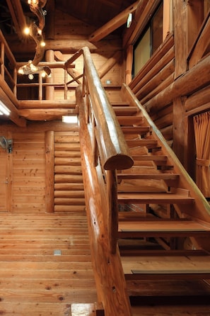 Un escalier en bois avec une rampe, des murs en bois et un plafond avec des poutres apparentes et des luminaires.