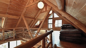 Un dormitorio rústico en el ático, con cama de altillo, vigas de madera y vistas por la ventana.