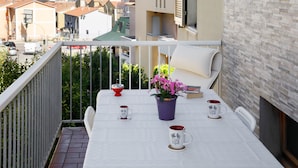 Ein Balkon mit Tisch für zwei Personen, mit einem Topfpflanzen, zwei Tassen und einer roten Schüssel.