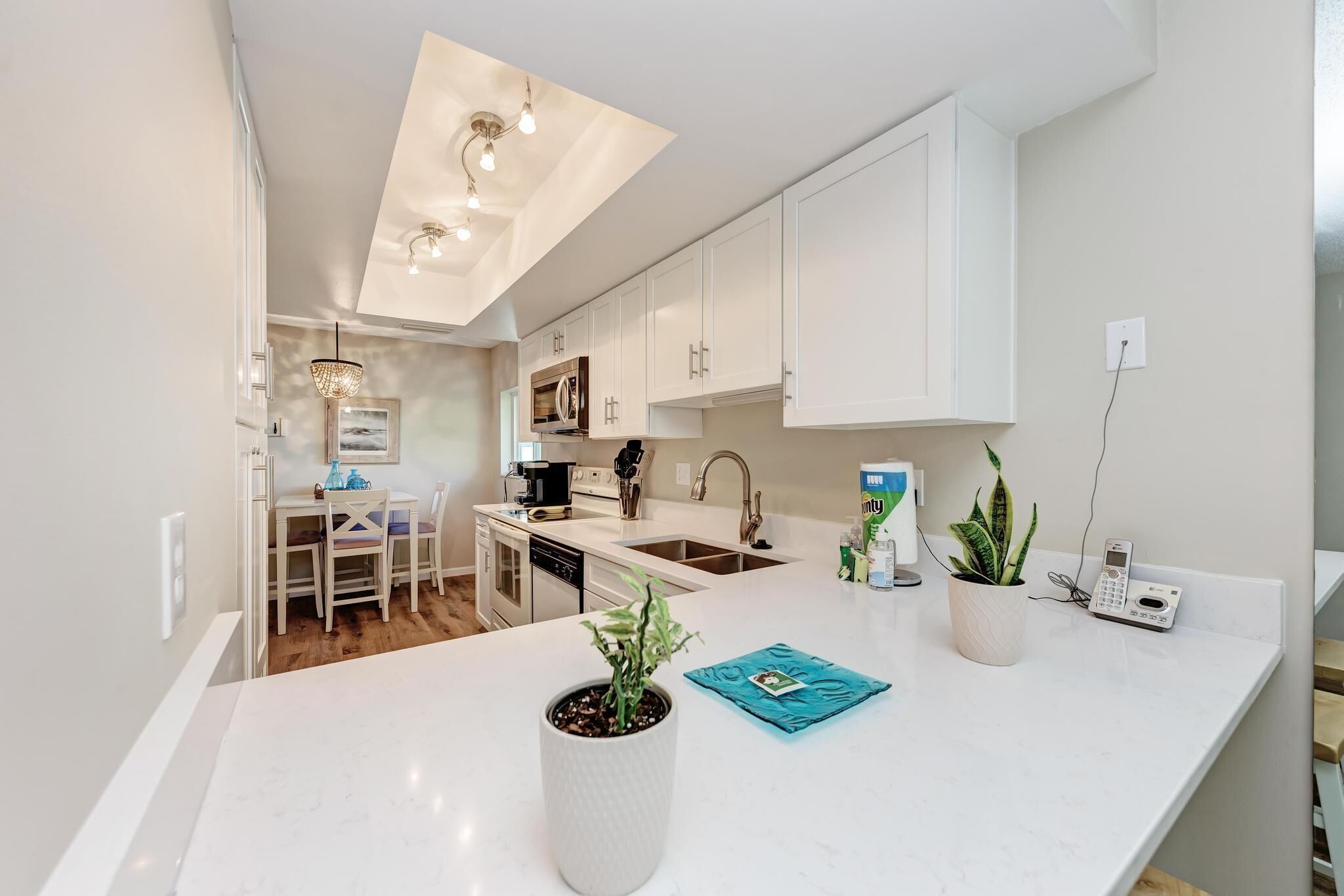 A modern kitchen with white cabinetry, a central island, and a dining area with a table and chairs.
