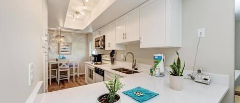 A modern kitchen with white cabinetry, a central island, and a dining area with a table and chairs.