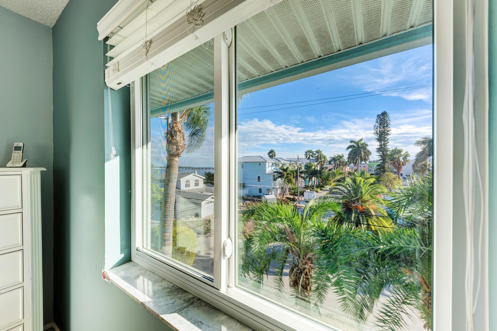 A room with a large window overlooking a residential area with palm trees and houses.