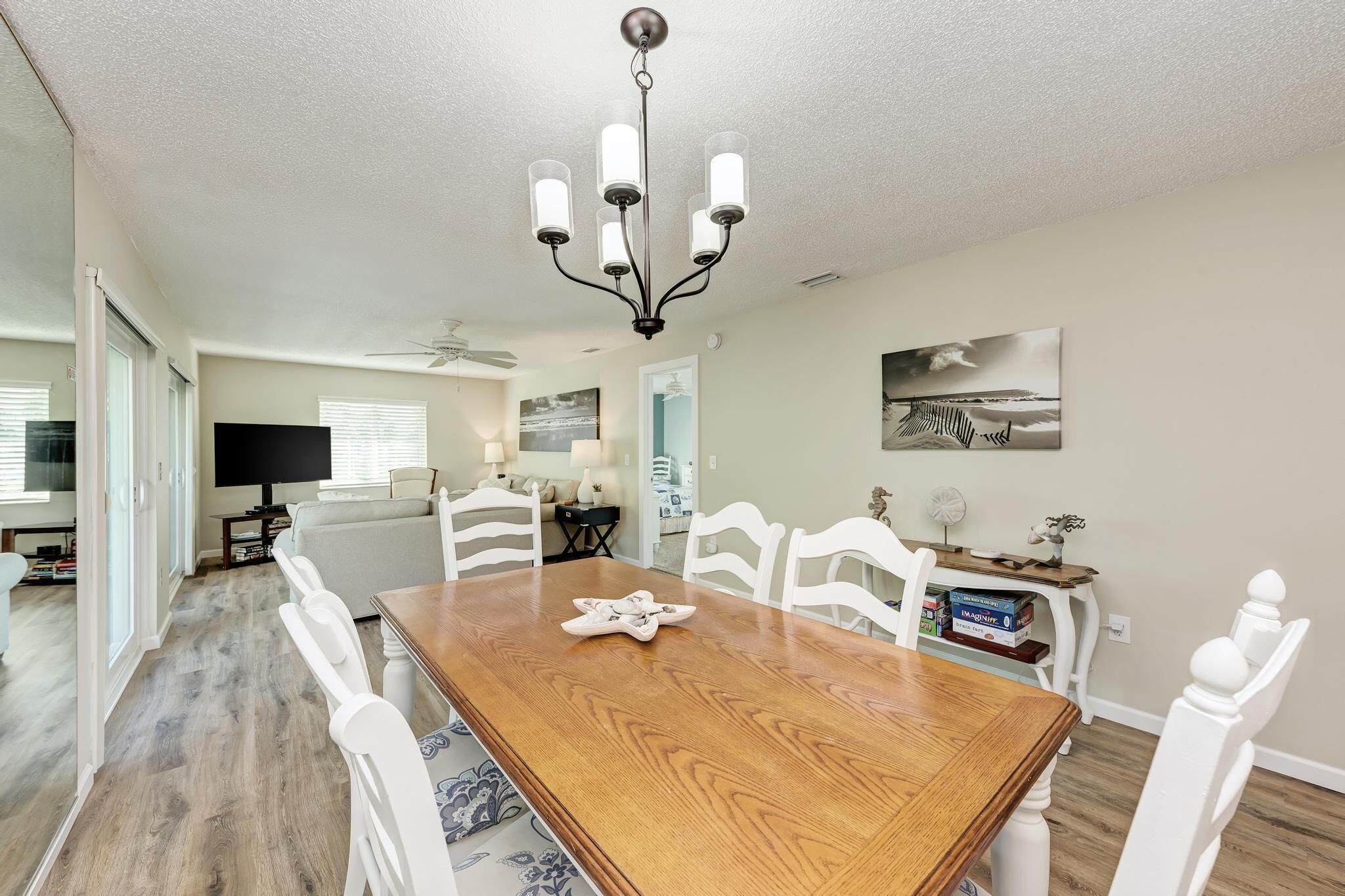 A dining area with a wooden table, white chairs, a chandelier, and a painting on the wall.