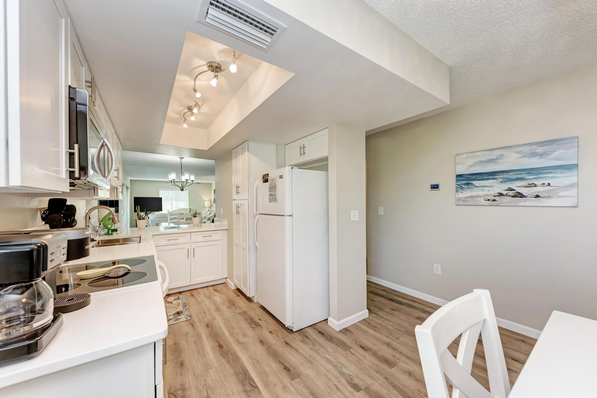 A modern kitchen with white cabinets, a built-in oven, and a refrigerator. There is a dining area with a table and chairs.