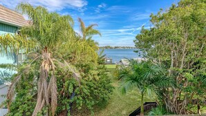 A view of a house with a large tree in the foreground, a body of water in the background, and a clear sky. - Anna Maria Island Beach Palms 8B (Bradenton Beach)