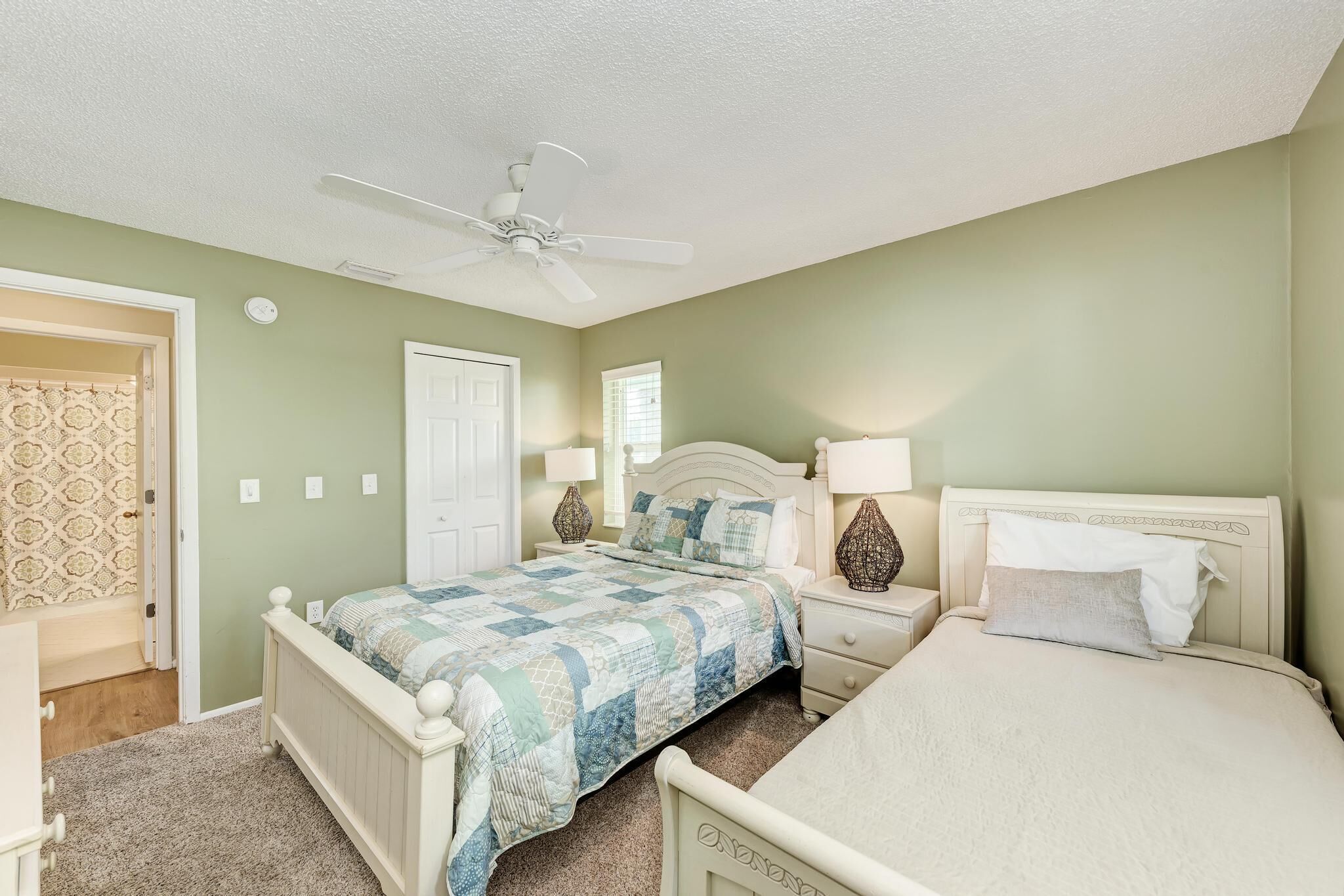 A bedroom with a bed, nightstands, a ceiling fan, and a door.