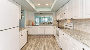 A modern kitchen with white cabinetry, granite countertops, and a wooden floor. - Anna Maria Island Beach Waves (Bradenton Beach)