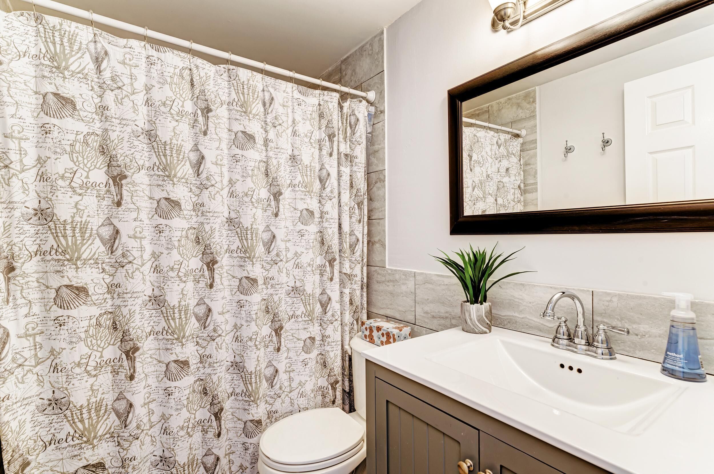 Un baño con cortina de ducha de temática náutica, un lavabo blanco con dispensador de jabón y un espejo sobre el lavabo.