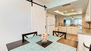 A dining area with a table set for two, a glass of dessert, and a sliding barn door leading to the kitchen. - Anna Maria Island Beach Waves (Bradenton Beach)