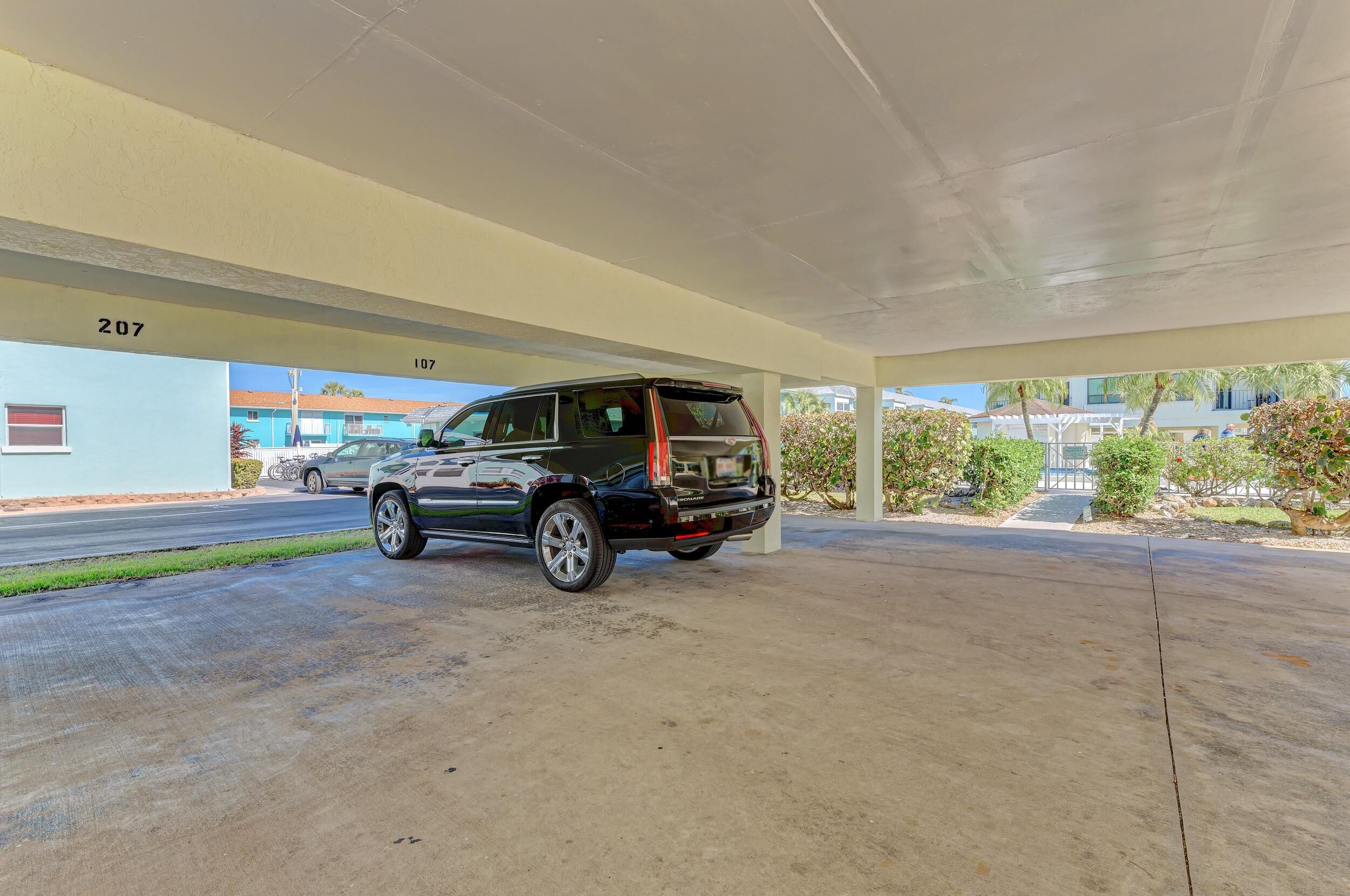 Un SUV negro estacionado bajo un área de estacionamiento techada con piso de concreto y un edificio al fondo.