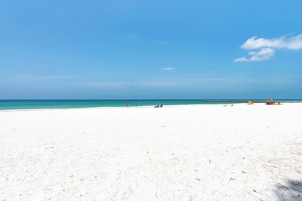 A wide sandy beach with a clear blue sky and calm sea. - AMI Gulf Lookout-views Of The Gulf From Every Room-rooftop Terrace (Bradenton Beach)