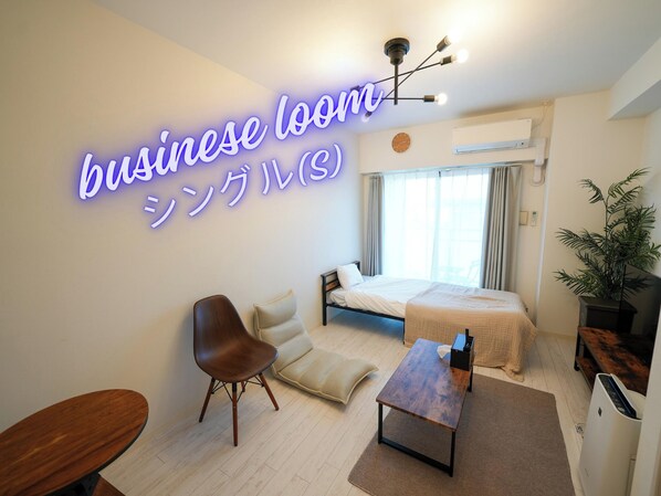 A modern hotel room with a bed, a desk, a chair, a plant, and a neon sign.