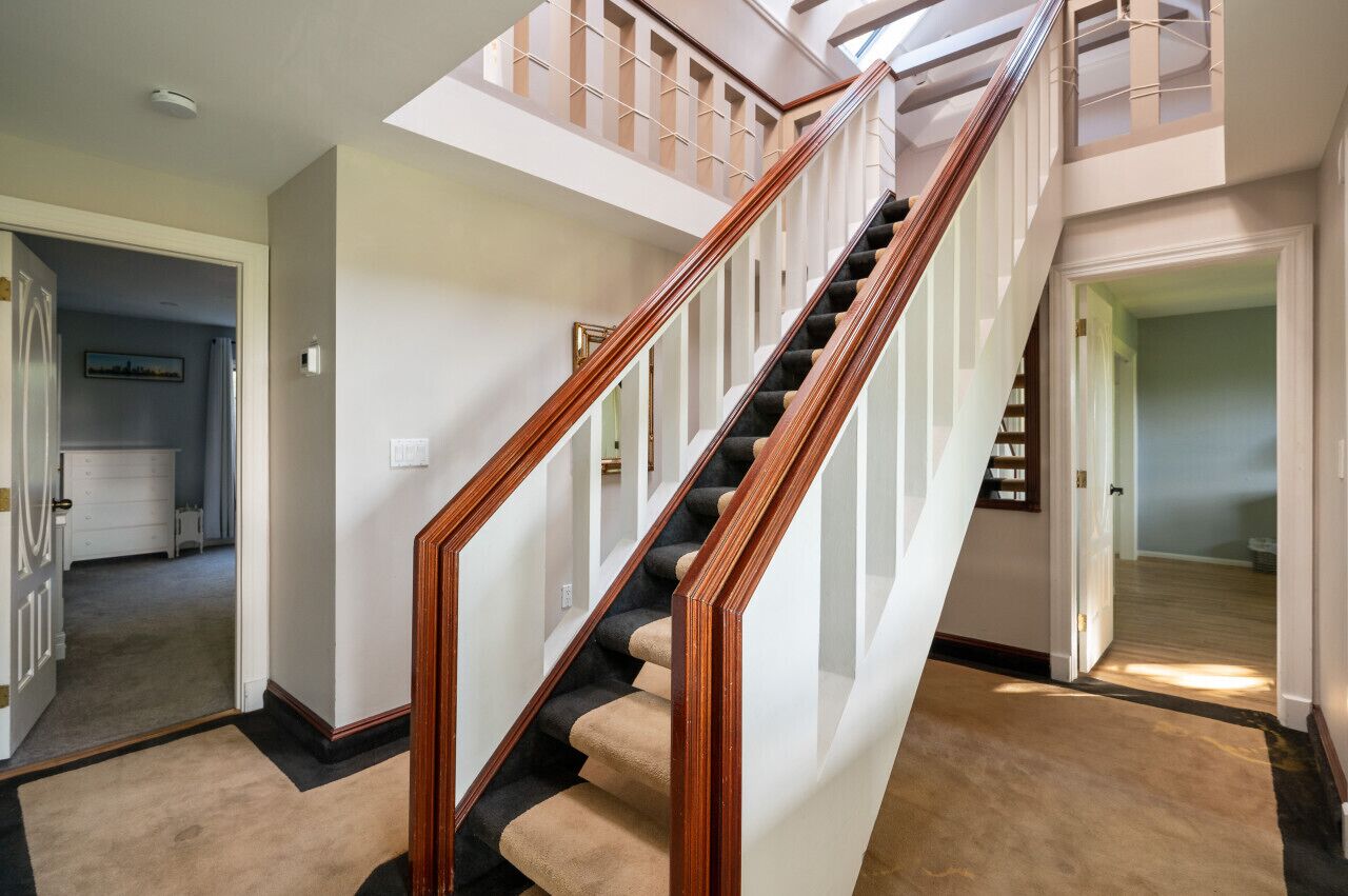 A staircase with wooden railings and beige carpeted steps leading to a second floor.