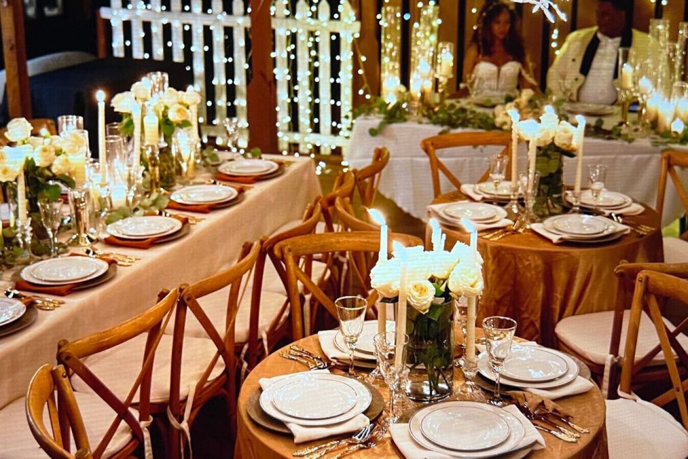 Une table dressée pour un repas formel, avec plusieurs couverts, de la vaisselle blanche, des verres et des bougies, le tout entouré de chaises en bois.