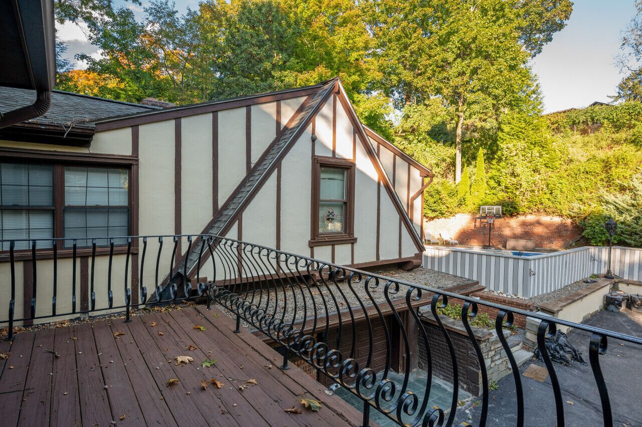 Una casa tradicional con techo inclinado, terraza de madera y barandilla de metal.