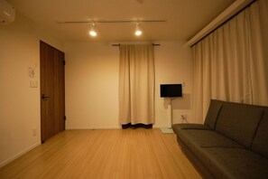 A room with a wooden floor, a brown door, a beige curtain, a black TV stand, and a brown sofa.