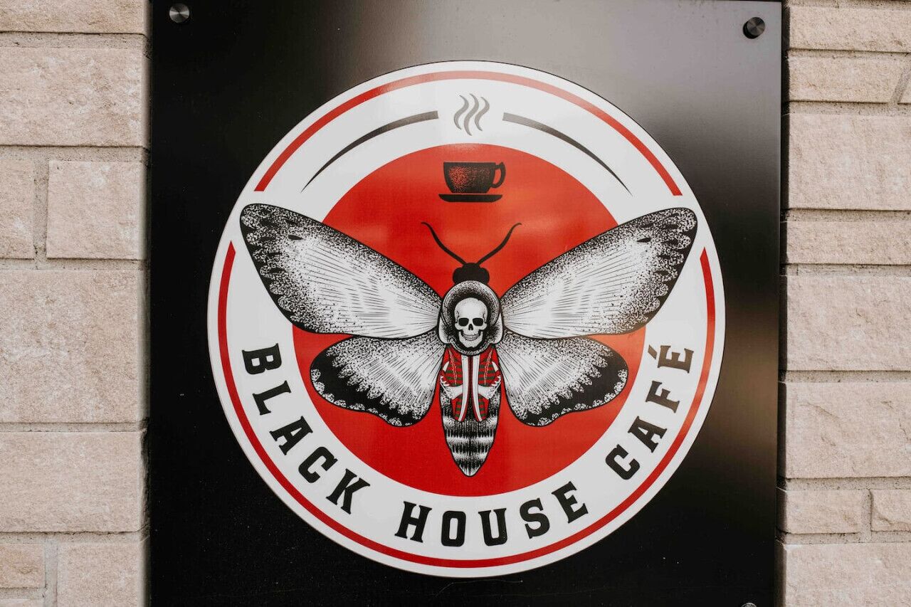 Een rond bord met een mot en een kop koffie, waarop staat 'Black House Café'.