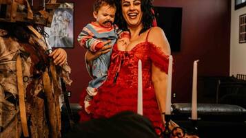 A room with a bed, a wooden structure, and a person in a red dress holding a child.