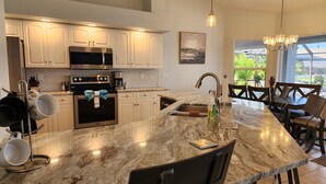 A modern kitchen with a large island, stainless steel appliances, and a dining area with a view.