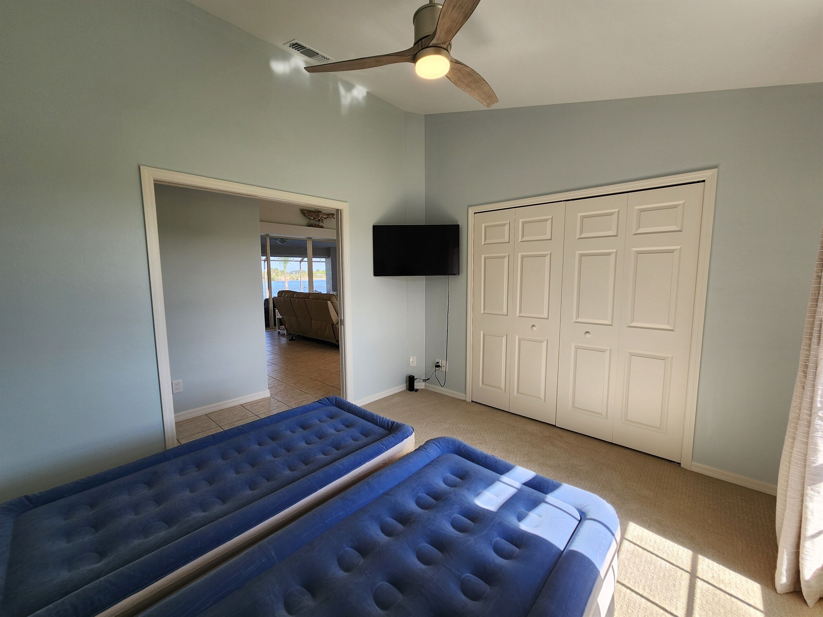 A room with two blue mattresses, a ceiling fan, a TV mounted on the wall, and a door leading to an outdoor area.