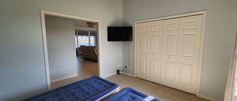 A room with two blue mattresses, a ceiling fan, a TV mounted on the wall, and a door leading to an outdoor area.