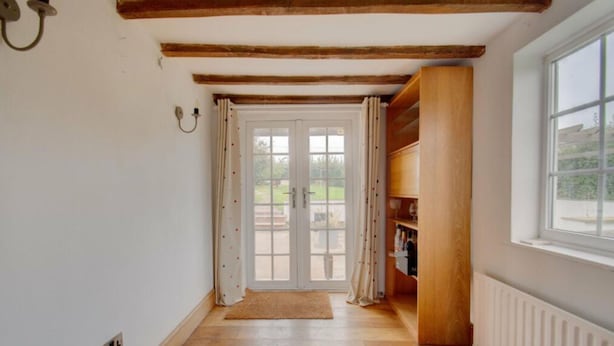 A hallway with a wooden floor, a white radiator, a wooden bookshelf, and a door leading outside. - Beautiful 3-bed House in the Hamlet of Ham Green (Redditch)