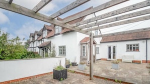A courtyard with a wooden pergola, white buildings with red-tiled roofs, and potted plants. - Beautiful 3-bed House in the Hamlet of Ham Green (Redditch)