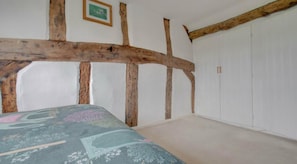 A bedroom with exposed wooden beams, a bed with a floral bedspread, and a white wardrobe.
