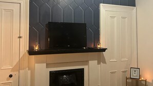 A room with a fireplace, a television on a mantel, and a wall with a geometric pattern.