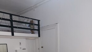 A room with a grey sofa, a glass table with two chairs, a white door, and a ceiling with string lights.