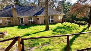 A brick house with a chimney, a fenced yard, and a tree in front.
