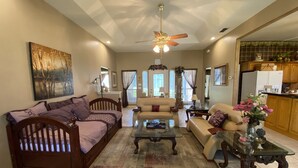 A spacious living room with a ceiling fan, a sofa, a coffee table, and a dining table with a vase of flowers.