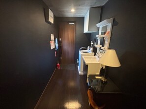 Un pasillo estrecho con una puerta de madera al fondo, un lavabo con espejo y una lámpara sobre una mesa.