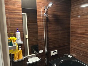 A bathroom with a wooden wall, a mirror, a handheld showerhead, a black bathtub, and toiletries on a shelf.