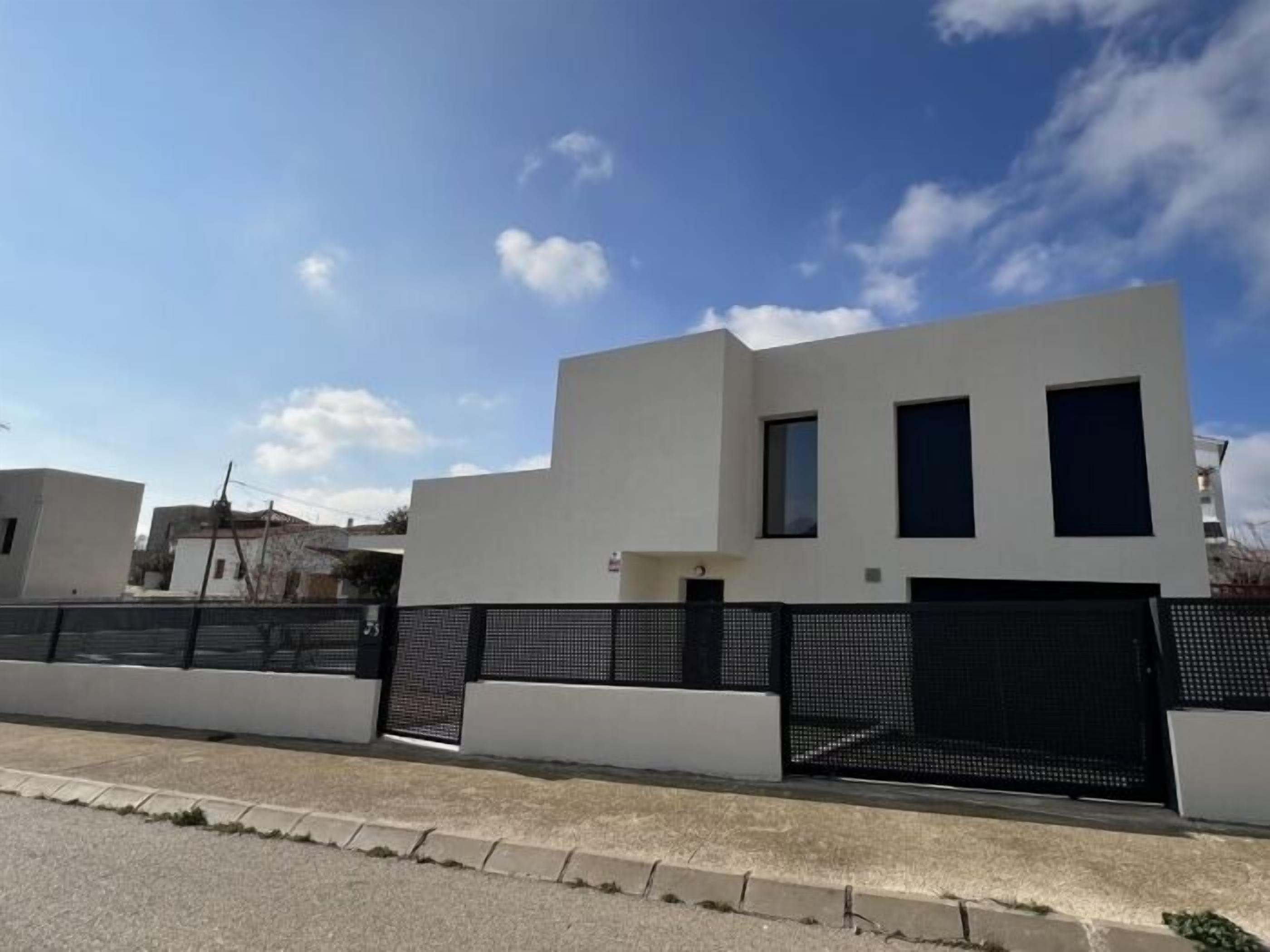 A modern building with a flat roof, a black gate, and a clear sky.
