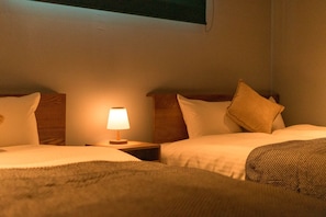 Habitación de hotel con dos camas, una mesita de noche con lámpara y una ventana sobre las camas.