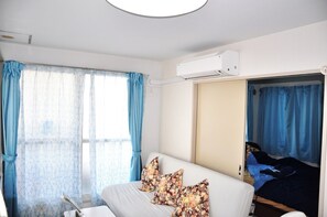 Une chambre d’hôtel avec un lit, une fenêtre avec des rideaux, un appareil de climatisation et une porte donnant sur une autre pièce.