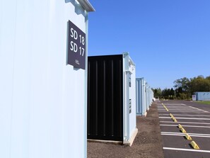 En række toiletvogne med skilte der angiver numre, en parkeringsplads med markerede pladser, og en klar blå himmel.