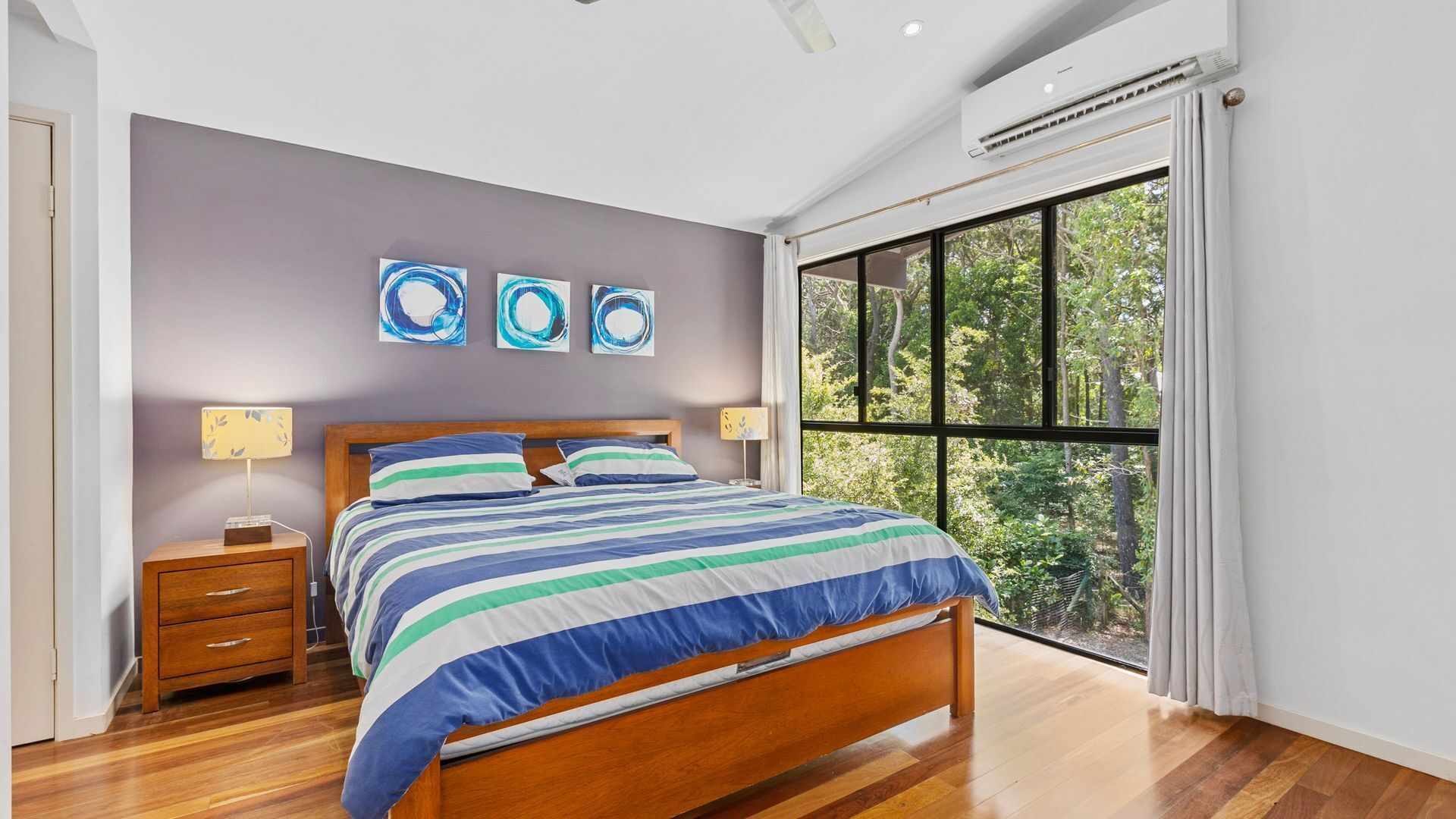 A bedroom with a bed, bedside tables, a window with a view of trees, and abstract wall art.