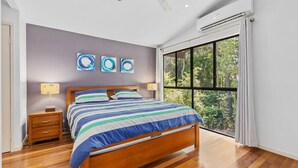 Une chambre à coucher avec un lit, des tables de chevet, une fenêtre donnant sur des arbres et des œuvres d’art abstraites accrochées au mur.