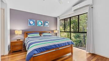 A bedroom with a bed, bedside tables, a window with a view of trees, and abstract wall art.