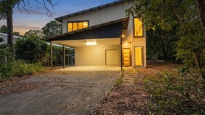 Une maison moderne dotée d’une allée couverte, d’un garage et d’un jardin bien entretenu.