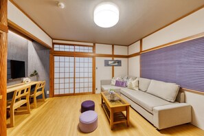Experience a serene retreat in this traditional Japanese-style living room, featuring a tatami mat floor, low table, and comfortable sofa.