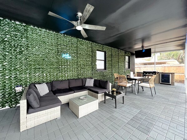 Un espace de vie extérieur moderne, doté d’un mur végétal, d’un ventilateur de plafond, d’un canapé et d’un barbecue.