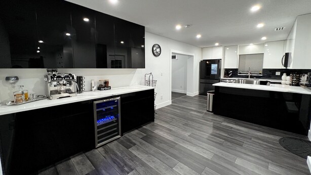A modern kitchen with black cabinets, a built-in oven, and a stainless steel refrigerator.